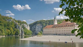 Das Kloster Weltenburg mit seinem Kieselstrand und der Donau, die  im Hintergrund durch den Donaudurchbruch hindurchfließt.