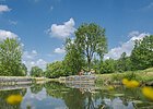 Am Ludwig-Donau-Main-Kanal der mittig fließt, haben es sich ein Pärchen am rechten Ufer in Liegestühlen gemütlich gemacht. Rechts und links stehen Bäume, der Himmel strahlt in blau.