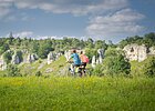 Radfahrer bei den 12 Apostel Solnhofen Zwei Personen fahren mit Fahrrädern auf einem grasbewachsenen Feld vor einer Felslandschaft.