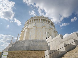 Befreiungshalle Kelheim Rundes, klassizistisches Gebäude mit Säulen und Statuen, umgeben von Treppen, unter blauem Himmel mit Wolken.
