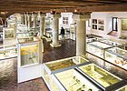 Museumsausstellung mit Vitrinen, archäologischen Funden und einer Person vor Säulen in historischem Gebäude